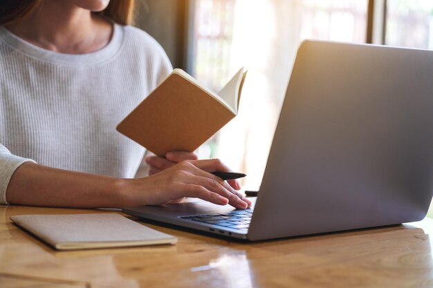 Imagem aproximada de uma mulher escrevendo em um notebook enquanto trabalhava em um laptop no escritório