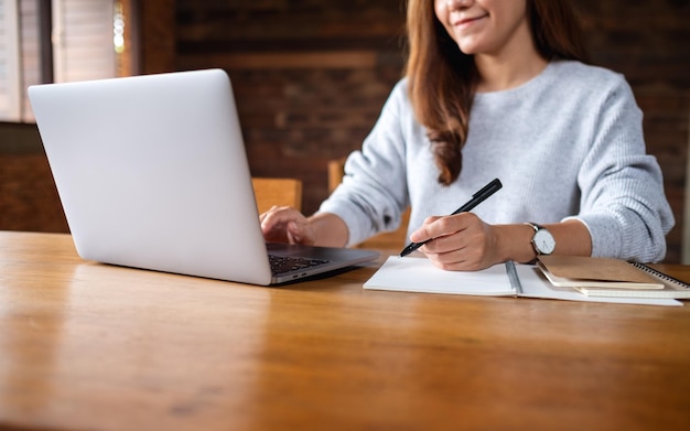 Imagem aproximada de uma mulher escrevendo em um notebook enquanto trabalhava em um laptop no escritório