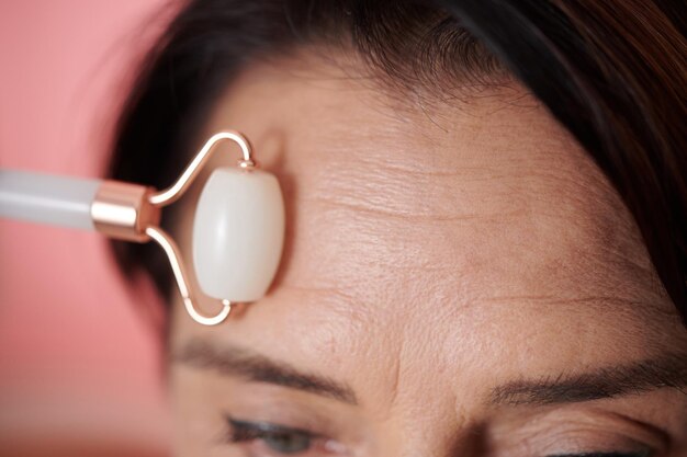 Imagem aproximada de uma mulher massageando a testa com rolo para reduzir o aparecimento de rugas