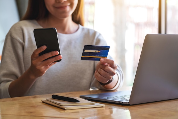 Imagem aproximada de uma mulher segurando cartão de crédito enquanto usa smartphone e laptop no escritório