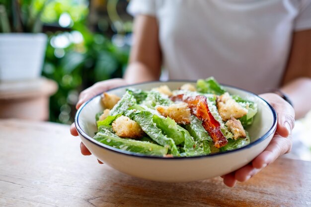 Imagem aproximada de uma mulher segurando e comendo uma salada caesar