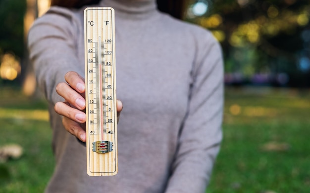 Imagem aproximada de uma mulher segurando e mostrando o termômetro ao ar livre