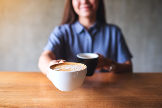 Imagem aproximada de uma mulher segurando e servindo duas xícaras de café quente