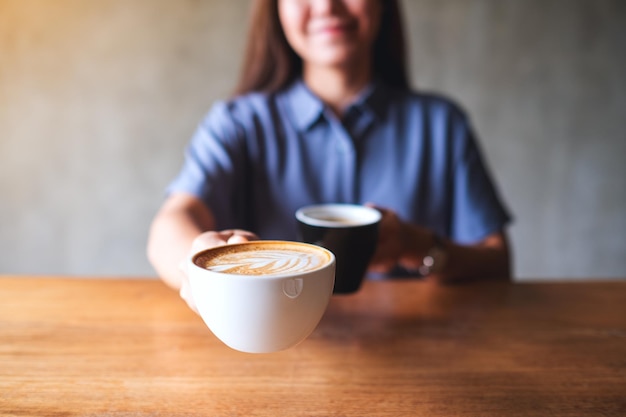 Imagem aproximada de uma mulher segurando e servindo duas xícaras de café quente