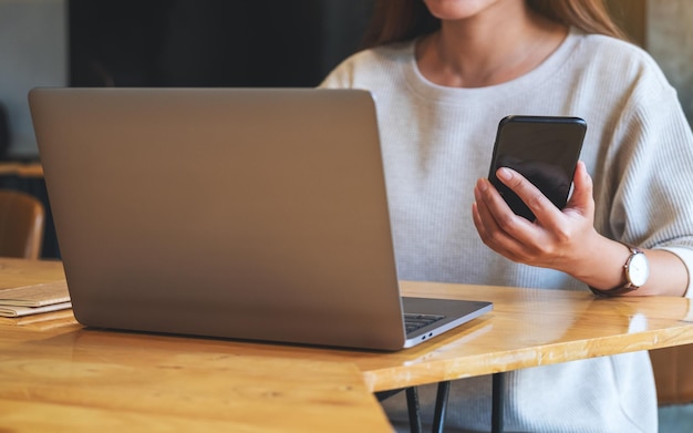 Imagem aproximada de uma mulher segurando e usando telefone celular e laptop no escritório