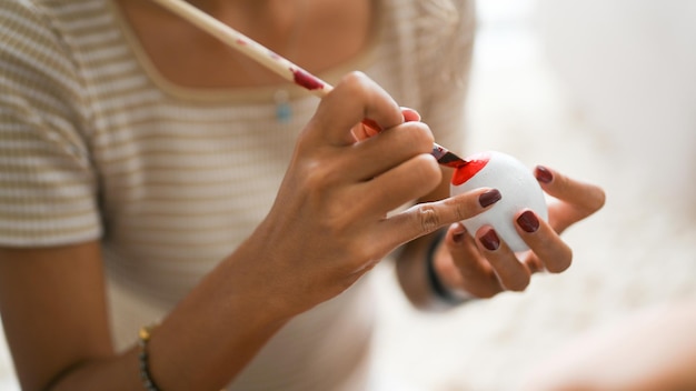 Imagem aproximada e mãos de foco Mãos femininas pintando em ovo de páscoa com cor vermelha feriado de páscoa