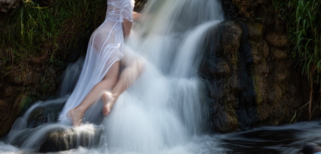 Imagem borrada de foco suave de mulher seminua em um vestido branco aprecia o frescor e o frescor dos jatos de água da cachoeira