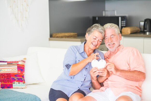 Imagem brilhante de casal de homem e mulher caucasianos felizes em casa sentados no sofá com cozinha brincando com uma lareira branca junto com amor