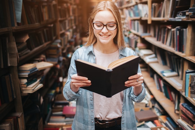 Imagem brilhante e quente de estudante inteligente, lendo um livro. A menina está sorrindo e continua a ler mais o livro.