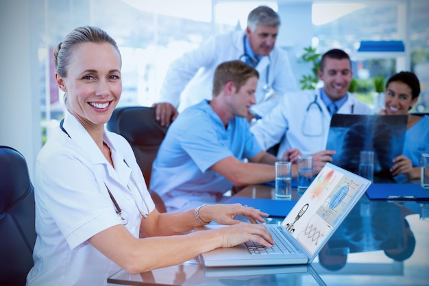 Foto imagem composta da bela médica sorridente digitando no teclado com sua equipe atrás