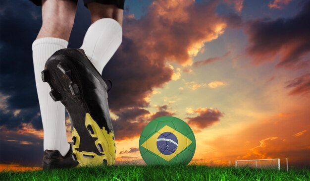 Imagem composta da bota de futebol chutando a bola do brasil contra a grama verde sob o céu azul escuro e laranja