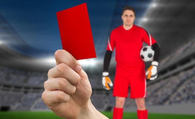 Foto imagem composta da mão segurando o cartão vermelho para o goleiro contra o estádio de futebol