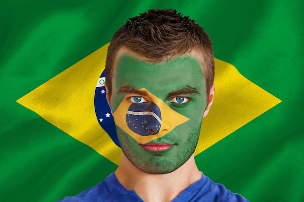 Imagem composta de jovem fã sério do brasil com pintura facial contra a bandeira nacional brasileira gerada digitalmente