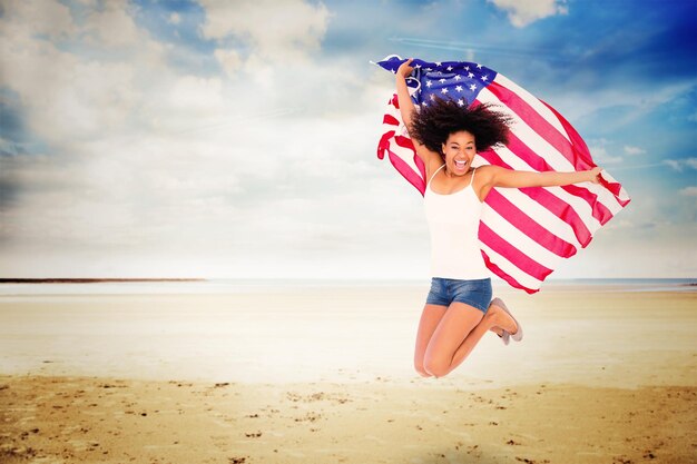 Imagem composta de menina bonita enrolada na bandeira americana, pulando e sorrindo para a câmera