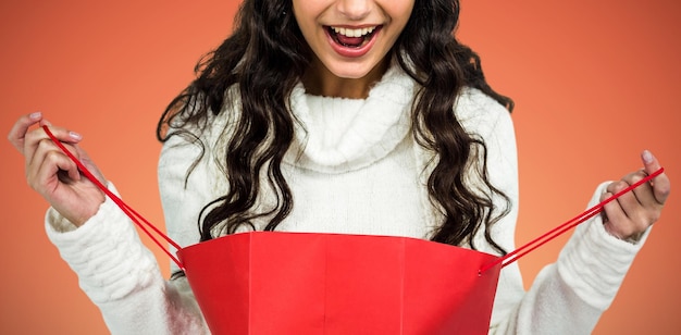 Imagem composta de mulher feliz com chapéu de Natal abrindo uma sacola de compras vermelha