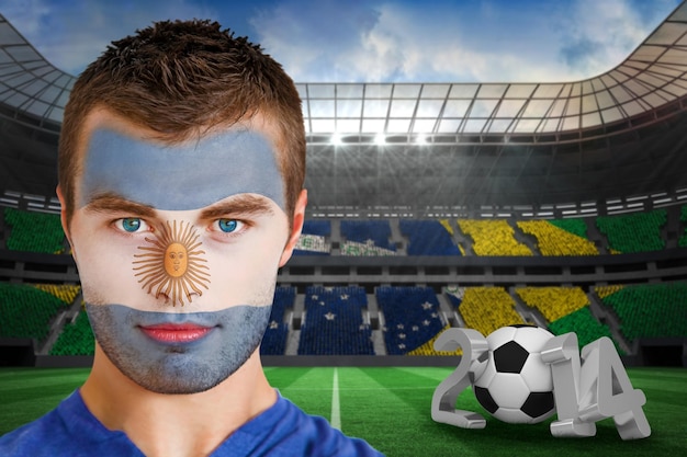 Foto imagem composta de sério jovem torcedor argentino com pintura facial contra grande estádio de futebol com torcedores brasileiros