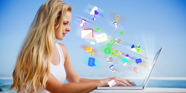 Foto imagem composta de uma linda loira usando seu laptop na praia contra ícones de aplicativos