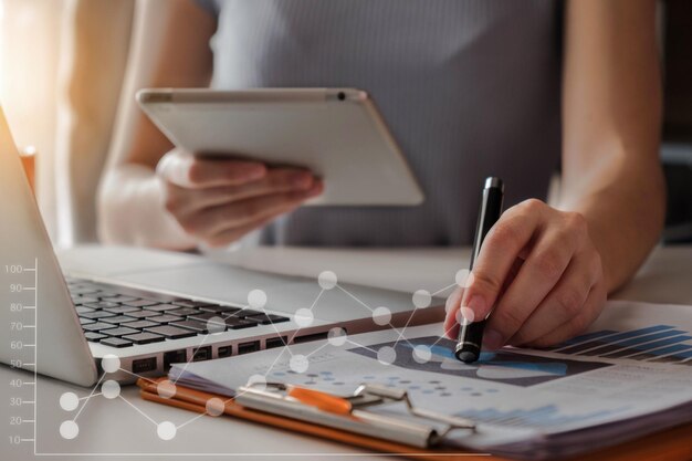 Foto imagem composta digital de mulher de negócios apontando para um gráfico enquanto usa tecnologias na mesa