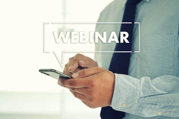 Imagem composta digital de um empresário usando telefone móvel com texto de webinar no escritório