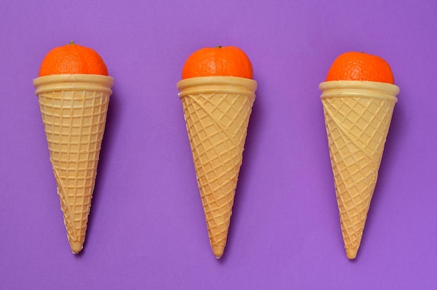 Imagem conceitual de sorvete três cones de waffle com tangerinas em um fundo roxo