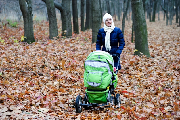 Imagem da jovem mãe com carrinho de bebê andando no parque outono.