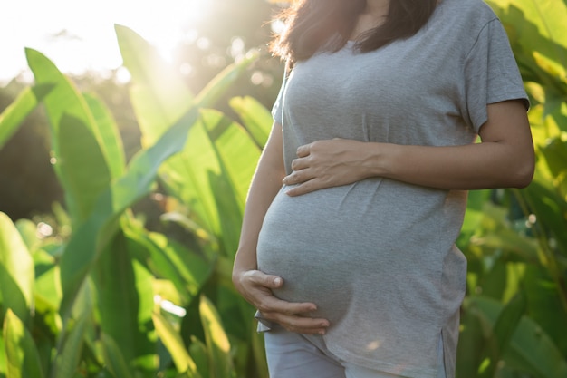 Imagem da jovem mulher grávida em pé ao lado das plantas