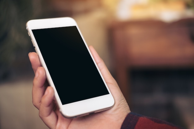 Imagem da maquete da mão segurando o celular branco com tela preta em branco no café