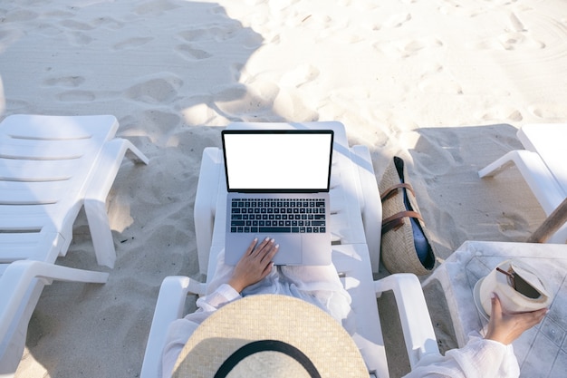 Imagem da maquete de vista superior de uma mulher segurando e usando um computador laptop com uma tela em branco enquanto se deita na cadeira de praia
