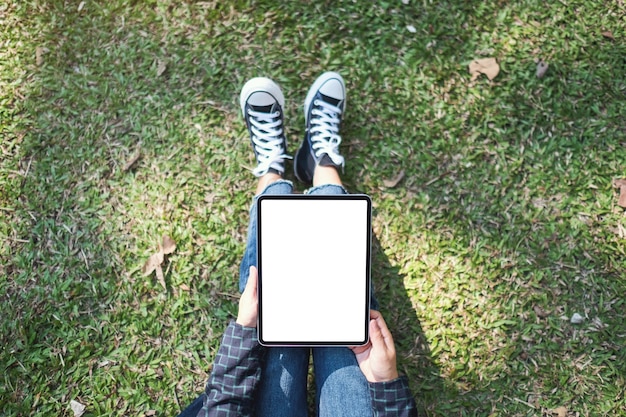 Imagem da maquete de vista superior de uma mulher segurando e usando um tablet pc preto com uma tela em branco enquanto está sentada ao ar livre