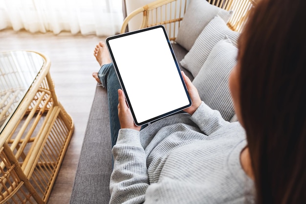 Imagem da maquete de vista superior de uma mulher segurando um tablet pc preto com uma tela em branco enquanto estava deitada em um sofá em casa