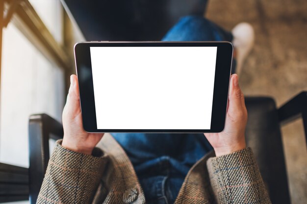 Imagem da maquete de vista superior de uma mulher sentada e segurando um tablet pc preto com uma tela de desktop em branco