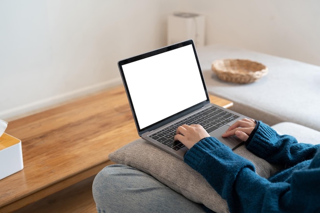 Imagem da maquete de vista superior de uma mulher trabalhando e digitando em um laptop com tela em branco, enquanto está sentada em um sofá em casa