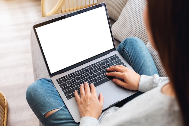 Imagem da maquete de vista superior de uma mulher trabalhando e digitando em um laptop com tela em branco, enquanto está sentada em um sofá em casa