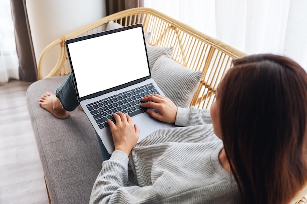 Imagem da maquete de vista superior de uma mulher trabalhando e digitando em um laptop com tela em branco, enquanto está sentada em um sofá em casa