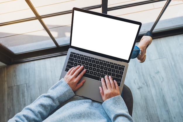 Imagem da maquete de vista superior de uma mulher usando e digitando em um laptop com uma tela de desktop em branco