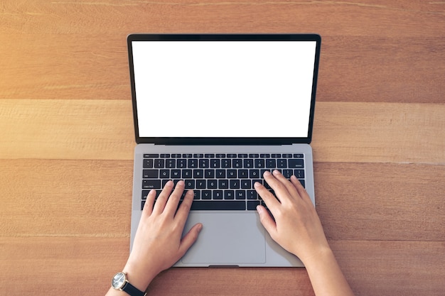Imagem da maquete de vista superior de uma mulher usando e digitando no laptop com a tela do desktop em branco na mesa de madeira no escritório