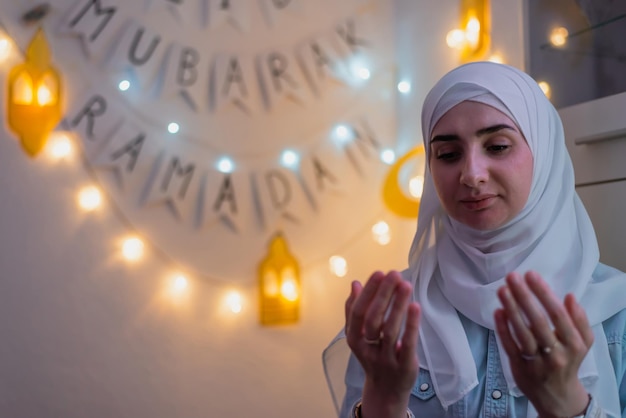 Imagem da mulher muçulmana rezando com as mãos para cima com decoração Mubarak Ramadan no fundo