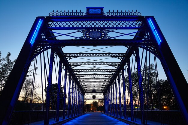 Imagem da ponte de metal brilha em azul quando iluminada por trás pelo sol poente