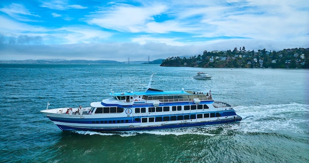 Imagem da vista lateral da Golden Gate Ferry com um barco menor perto de Tiburon e da Golden Gate Bridge em uma distância aérea