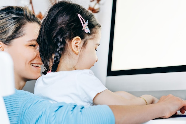 Foto imagem da vista traseira da mãe loira feliz sentada com a filha em casa e trabalhando jovem mulher com criança pequena trabalhando no computador e brincando de mãe dona de casa aprendendo com seu filho