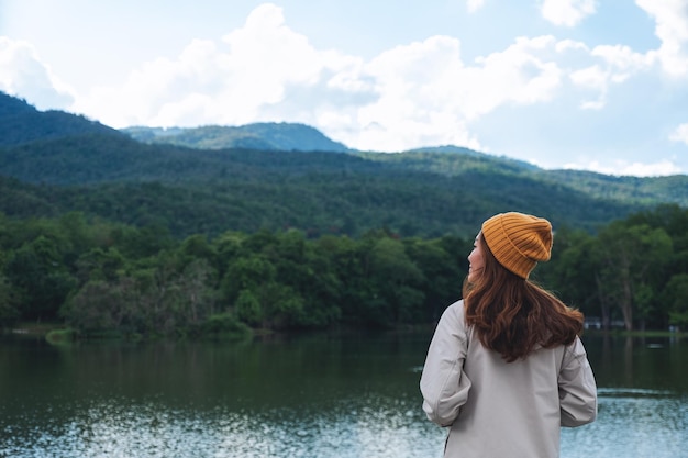 Imagem da vista traseira de uma mulher olhando para belas montanhas verdes à beira do lago