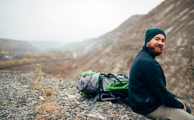 Imagem da vista traseira do jovem caminhante feliz de chapéu verde se sentir bem depois de caminhar nas montanhas Viajante barbudo masculino sorrindo e se sentindo feliz durante o trekking em sua jornada Estilo de vida de viagem