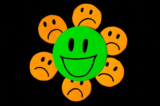 Foto imagem de alguns emoticons recortados de papel laranja com um rosto triste em torno de um grande emoticon verde com um rosto sorridente conceito de más influências más amizades negatividade problemas bullying