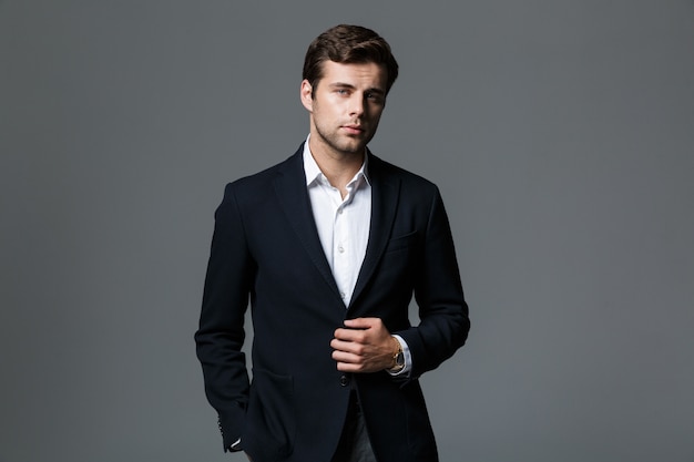 Imagem de atraente empresário de 30 anos em jaqueta preta isolada sobre uma parede cinza