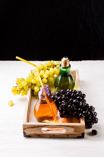 Imagem de bandeja de madeira com uvas verdes e pretas, duas garrafas de suco