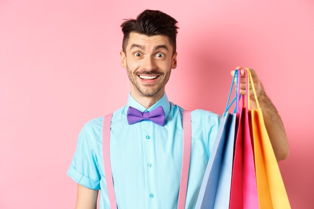 Imagem de cara feliz em compras, segurando sacolas de papel e sorrindo animado, comprador comprando com descontos, de pé na rosa.