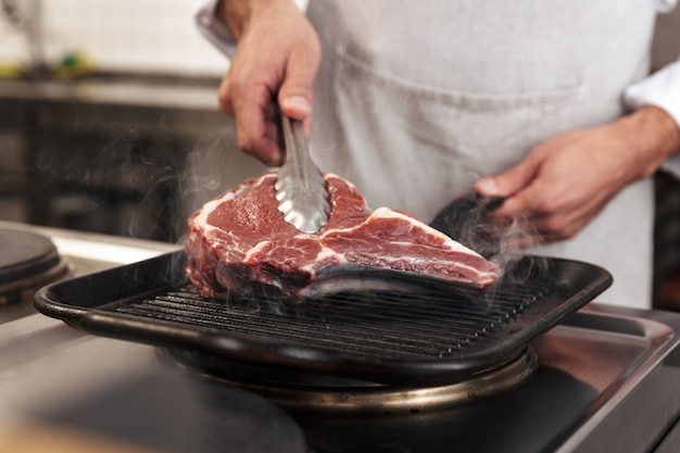 Imagem de chefe masculino europeu em uniforme branco, grelhados na cozinha em restaurante