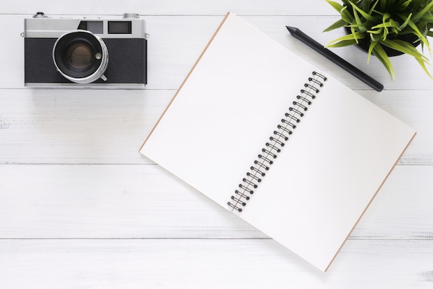 Imagem de cima de um caderno aberto com páginas em branco e câmera em uma mesa de madeira