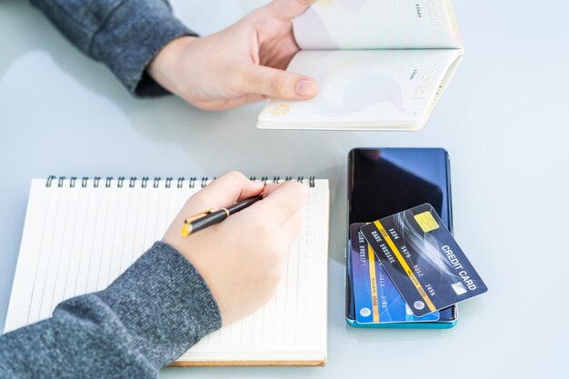 Imagem de close de mulher escrevendo em um caderno com cartão de crédito e mesa de smartphone