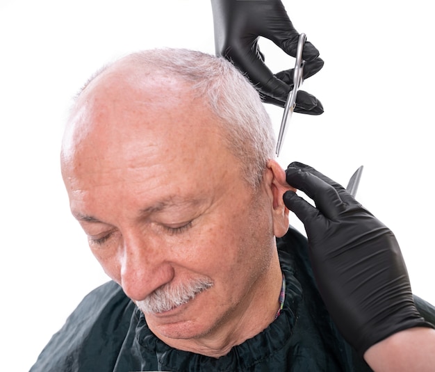 Imagem de close de um homem sênior na barbearia. Barbeiro cortando o cabelo com uma tesoura